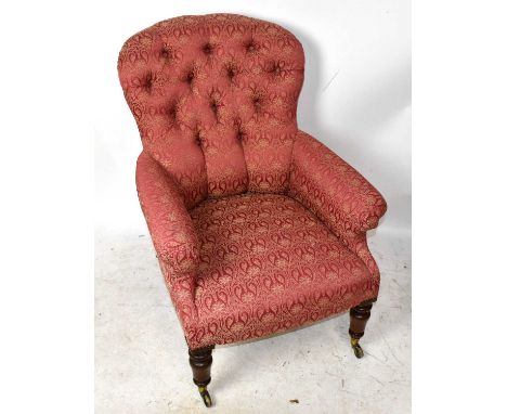 A Victorian armchair upholstered with button back red and gilt floral material on turned column supports terminating on brass