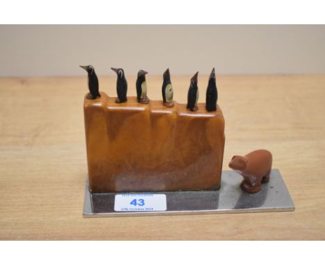 An Art Deco cocktail stick set, the bakelite holder containing six carved wooden penguin picks beside a polar bear, all raise