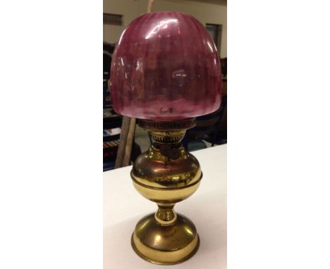 A vintage oil lamp with cranberry glass shade.