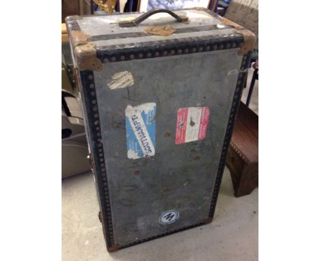 A large vintage grey travelling trunk with destination labels.