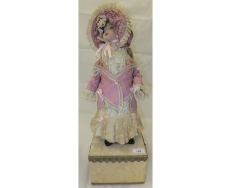 A bisque headed musical automaton doll wearing cream dress and pink jacket and bonnet