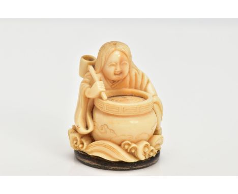 A CHINESE IVORY NETSUKE, a small carved ivory netsuke depicting a person at a cooking pot, floral detailing on the kimono and