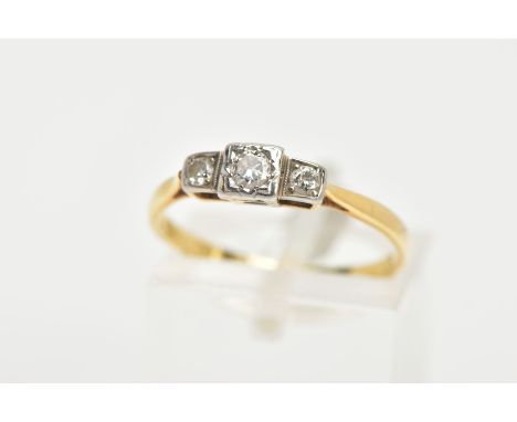 A YELLOW METAL THREE STONE DIAMOND RING, centring on a round brilliant cut diamond within a square mount, flanked with two mo