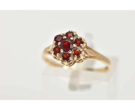 A 9CT GOLD GARNET CLUSTER RING, flower cluster set with seven circular cut garnets, prong set, trifurcated shoulders leading 