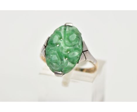 A JADEITE RING, an oval carved jadeite panel set in a white metal with tapered shoulders leading on to a yellow metal band, j