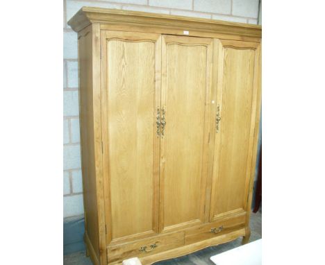 A Light oak French style triple wardrobe with a cavetto cornice above three panelled cupboard doors , two drawers and curvili