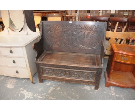 An Early 20th Century carved oak monks bench the hinged top centred with an incised coat of arms above a box seat and a front