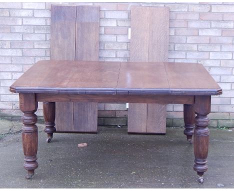 A late Victorian oak extending dining table, the rectangular top with canted corners on turned reeded legs with ceramic casto
