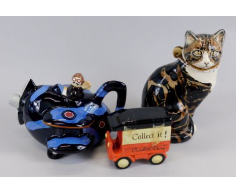 A Carlton ware ceramic model teapot of a bi-plane, a Carlton ware bus and a studio pottery cat, (3). 