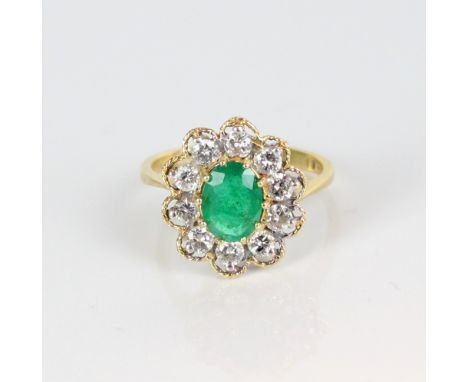 18ct yellow gold emerald and diamond cluster ring, the central oval cut emerald surrounded by a halo of brilliant cut diamond