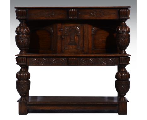 A joined oak buffet, 17th Century style, the top supported on carved bulbous cup and covers, central arcaded door under, flan