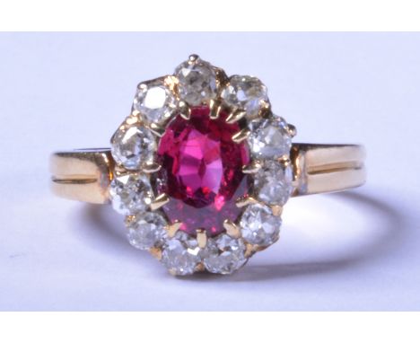 A ruby and diamond oval cluster ring, yellow metal two strand shank and shoulders, the oval mixed cut ruby surrounded by ten 