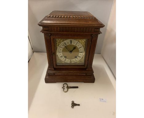 AN OAK CASED CHIMING MANTLE CLOCK WITH DECORATIVE GILT FACE WITH ROMAN NUMERALS COMPLETE WITH BOTH KEYS 