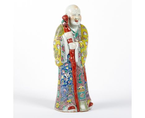 Chinese porcelain figure of an immortal holding a staff. His garments are decorated with vibrantly colored enamels in several