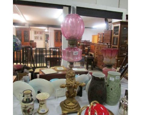An oil lamp with cranberry font and shade being supported by a lion
