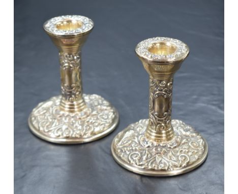 A pair of Elizabeth II silver candlesticks, having embossed decoration and step moulding to the scones, further embossed deco