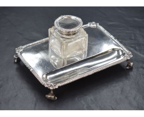 A George V silver inkwell stand, of rectangular form having scroll and gadrooned rim, with a square silver mounted glass inkw