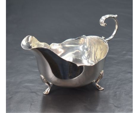 A George V silver sauce boat, having a Chippendale style rim and generous spout opposed by a s-curve scroll handle, raised on
