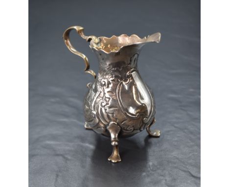 A Georgian silver cream jug, of bulbous form having a Chippendale style rim, shallow spout opposed by a scroll handle with a 