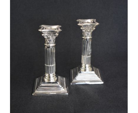 A pair of George V silver Corinthian column candlesticks, having concave square detachable sconces with bead trim, embossed d