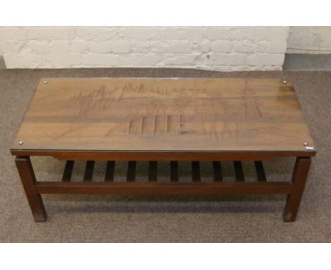 A teak glass top two tier coffee table with carved oriental scene and magazine shelf.