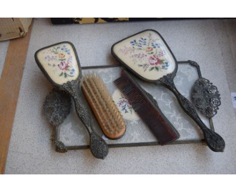 An early 20th century ladies' vanity set with filigree work and floral embroidery backs, comprising mirror, two brushes, comb