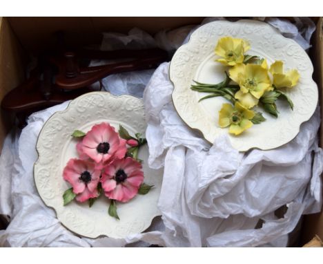 A collection of floral ceramic decorative plates, including a set with sculpted flower bouquets in the centre and a number of