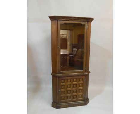 A modern Ercol style oak standing corner cabinet, with single glazed door above a door with twelve small panels on a plinth, 