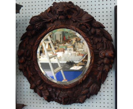 A Black Forest type carved wall mirror, decorated overall with fruit, lion masks etc., and with a circular bevelled plate, 69