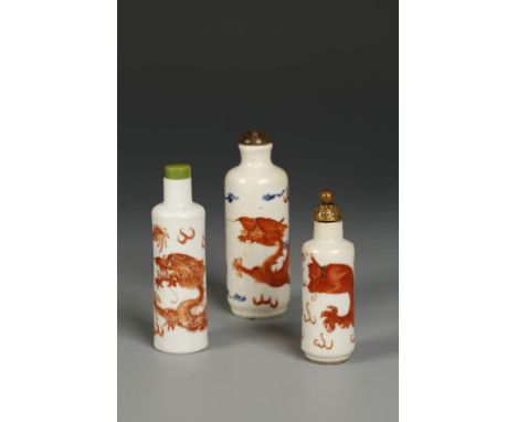 THREE CHINESE PORCELAIN CYLINDRICAL SNUFF BOTTLES decorated in iron red with dragons, the larger example also with blue ename