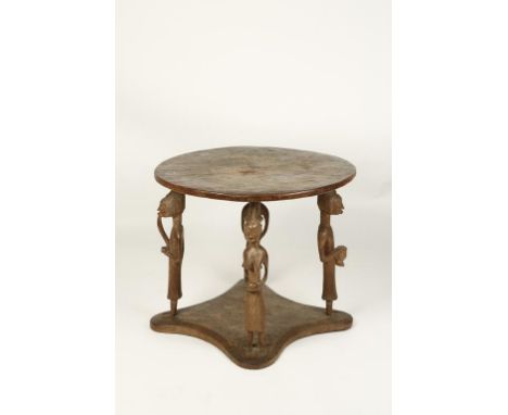 A WEST AFRICAN TRIBAL HARDWOOD TABLE, the circular top on four figural supports, two male and two female, one smoking a pipe,