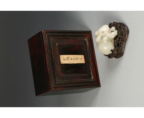 A CHINESE CELADON JADE HARE, the recumbent creature holding a lingzhi spray in its' mouth, 2.25" long, on a hardwood stand an