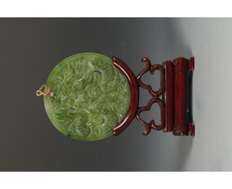 A CHINESE GREEN JADE PENDANT carved with a dragon and phoenix, late Qing/Republic, 2.5" dia., on a wooden stand