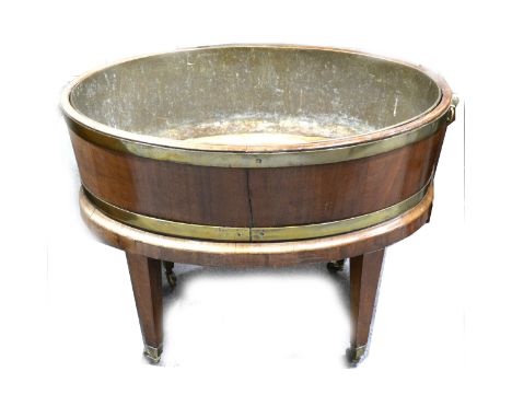 A George IV mahogany wine cooler, oval section with brass bands, and loose-ring handles, brass liner, on stand, square taperi