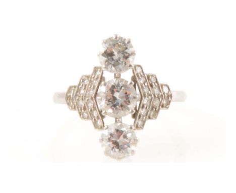 A diamond three stone ring in the Art Deco style, the three brilliant cut diamonds claw set vertically in an all white metal 