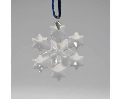 Swarovski crystal snowflake ornament from 1999, featuring a delicate multi-faceted star design suspended on a blue ribbon. In