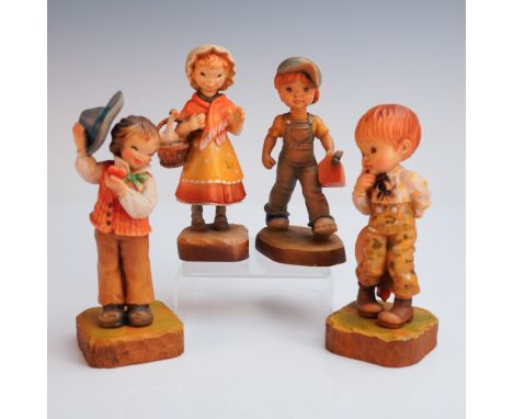 A delightful set of four ANRI hand carved wood figurines, each radiating playful charm. One boy lifts his blue brimmed hat wh