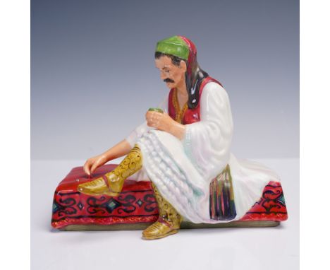 This ceramic figurine titled Albanian Dice Thrower features a seated man in traditional Albanian attire, poised mid-game on a