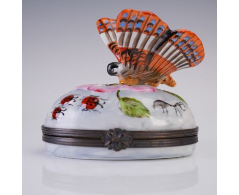 Hand-painted oval porcelain trinket box featuring a vivid sculptural butterfly finial poised above a garden scene of red lady