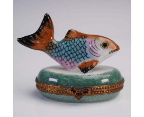 Hand-painted Limoges porcelain trinket box in the form of a vibrantly colored fish perched on a green oval base. The base ope