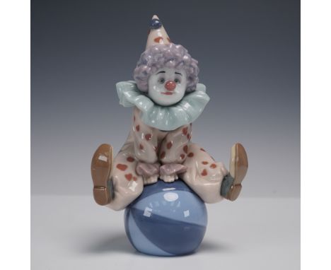 Delightful Lladro porcelain figurine featuring a cheerful clown seated playfully atop a glossy blue ball. The clown wears a s
