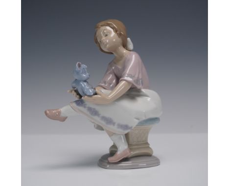 Charming Lladro porcelain figurine depicting a young girl seated on a decorative stool, gently holding her beloved blue teddy