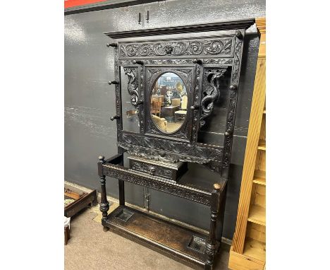 Late Victorian gothic carved hall stand with central oval mirror and glove drawer, extensively carved throughout, 120cm wide