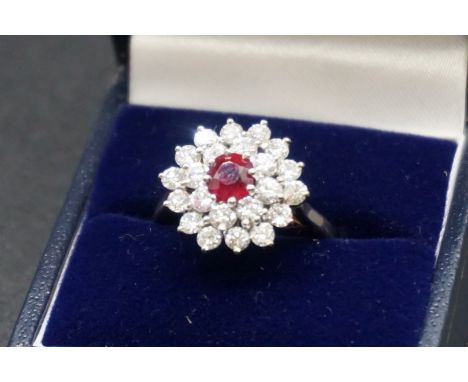 A white metal ruby and diamond cluster ring, stamped 18ct, set central oval claw set ruby surrounded by two rows of claw set 