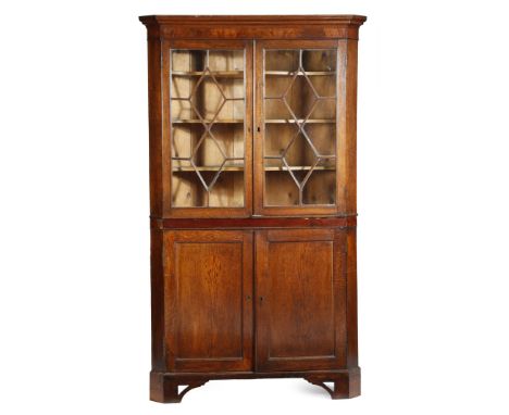 A George III oak standing corner cupboard, with mahogany banding, with a pair of astragal glazed doors, enclosing three shape