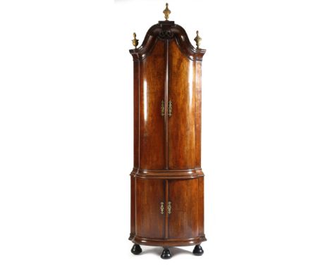 An 18th century Dutch walnut standing corner cupboard, with a domed scroll cornice and three carved giltwood finials, above a