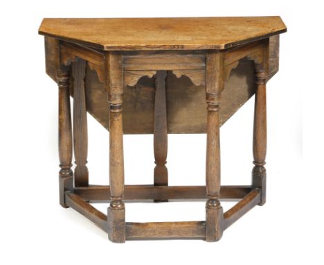 A 17th century style oak credence type table, the canted top with a hinged drop-leaf on a gate support, on turned legs united