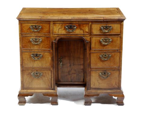 A George II and later walnut kneehole desk, the crossbanded top with a moulded edge, above an arrangement of nine drawers, wi