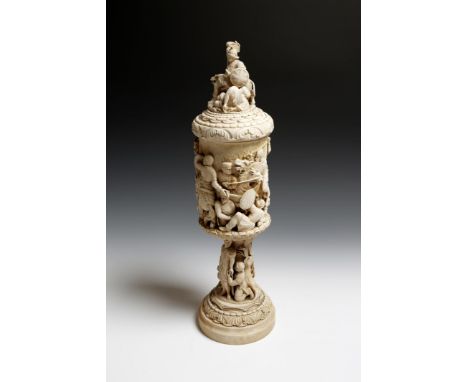 λ A large late 19th century German ivory carved cup and cover, with a victorious warrior and lion finial, the body of the cup