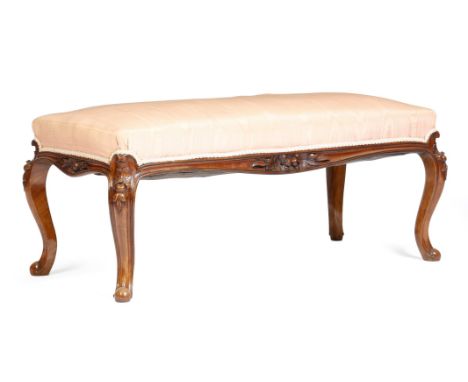 A Victorian walnut long stool, the seat upholstered with pink watered silk, the frieze carved with leaves and flowers on conf